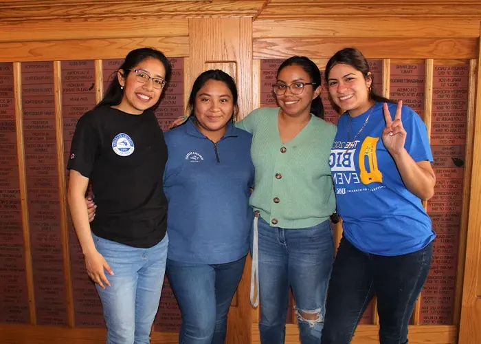 trio students pose for a photo in front of a wood paneled wall